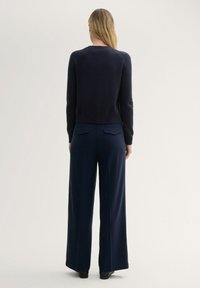 Marineblauer, kurz geschnittener Pullover mit langen Ärmeln, kombiniert mit weit geschnittenen marineblauen Hosen mit zwei Gesäßtaschen. Weiche Textur und minimales Design.