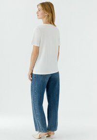 Witte T-shirt met korte mouwen, gecombineerd met lichtblauwe, hoog geplaatste, wijd uitlopende jeans; gladde stof; eenvoudig ontwerp; minimalistische stijl.