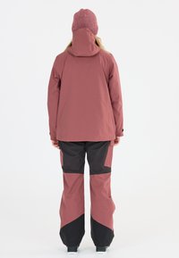Wasserdichte, zweifarbig gestaltete Ski-Jacke in Pink und Schwarz mit Kapuze, kombiniert mit passenden Ski-Hosen in Pink und Schwarz. Glattes, robustes Material.