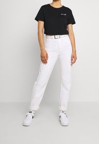 Černé tričko s krátkým rukávem s nápisem "smile", spárované s ohrnutými bílými džíny a bílými teniskami s černými akcenty.