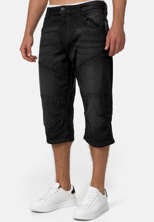 Pantalones capri de mezclilla negra con forma tapered, superficie texturizada y costuras en contraste. Combinados con zapatillas blancas.