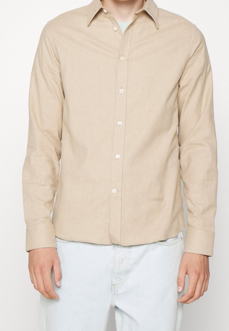 Beige overhemd met lange mouwen, knoopsluiting, klassieke kraag, gestructureerde stof en subtiele branding op de onderzoom. Voorkant met knoopsluiting.