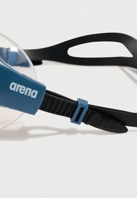 Blå og svart justerbar svømmebrille-rem med klar linse-seksjon og "arena" merkevare på siden.