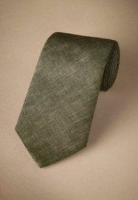 Cravate verte texturée, fabriquée en tissu, avec une extrémité effilée et une forme enroulée. Design à tissage plat avec des variations de couleur subtiles.