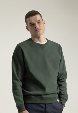 Sudadera verde de material suave, con cuello redondo, mangas largas, puños acanalados y un pequeño logo en el pecho. Capa base blanca visible.