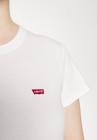 Fehér pamut póló, kerek nyakkivágással és rövid ujjakkal, a bal mellrészen piros hímzett Levi's logóval.