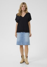 Haut en tricot noir à manches courtes avec un col en V, associé à une jupe en denim bleu clair et des bottines en cuir beige. Design simple avec des couleurs classiques.