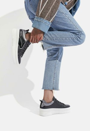 Sneaker basse nere e argento con parte superiore testurizzata, suola platform bianca e chiusura con lacci, indossate con jeans blue strappati.
