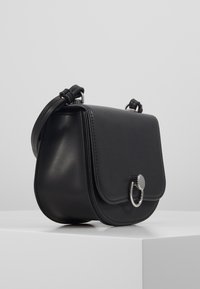 Borsa a tracolla in pelle nera dalla forma arrotondata, con pattina frontale, accessori in argento e una tracolla intrecciata. Texture liscia con dettagli minimi.