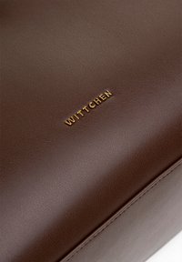 Borsa in pelle marrone con superficie texture, grana sottile e logo "WITTCHEN" in oro stampato sul davanti. Bordo e cuciture lisci visibili.