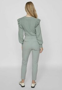 Vaaleanvihreä ribbipaita, jossa on frillakoristeita hartioilla, yhdistettynä sopiviin kapeisiin housuihin. Tasapohjaiset kengät viimeistelevät asun.