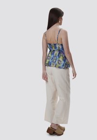 Top peplum floral en azul, amarillo y verde con tirantes finos; combinado con pantalones de pierna ancha en crema; zuecos marrones con acentos de tachuelas.