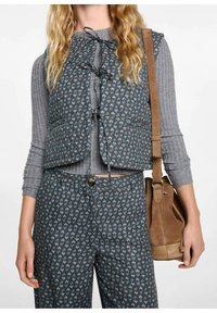 Niebieska kamizelka w wzory z zapięciem na krawat, noszona na szarym, prążkowanym topie; zestawiona z dopasowanymi spodniami w ten sam wzór oraz brązową skórzaną torebką na ramię.