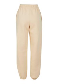 Beige Baumwoll-Sweatpants mit einem elastischen Bund, seitlichen Taschen und gerippten Säumen an den Knöcheln. Glatte Textur über die gesamte Hose.