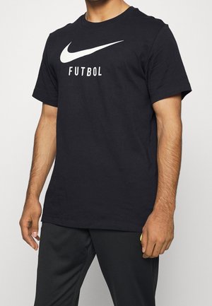 Persona con una camiseta negra de Nike con el logo swoosh blanco y el texto "FUTBOL", combinada con pantalones negros.