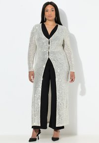 Abrigo duster de lentejuelas plateadas con mangas largas y cierre de botón en el frente, combinado con una blusa y pantalones negros. Textura suave, diseño hasta el suelo.