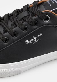 Czarne skórzane sneakersy z teksturowaną powierzchnią, białą gumową podeszwą i czarnymi sznurówkami. Zawierają logo "Pepe Jeans London" w białym kolorze po boku.