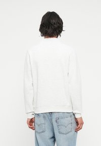 Sudadera gris claro, con cuello redondeado, mangas largas, puños y dobladillo de canalé, textura suave, combinada con jeans de corte holgado en azul claro.