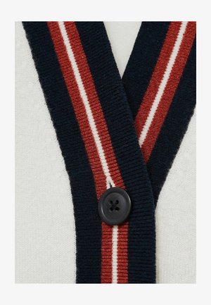 Sweter kardigan z granatowymi i czerwonymi paskami na kremowym tle; ma duży czarny guzik, dzianinową strukturę oraz dekolt w serek.