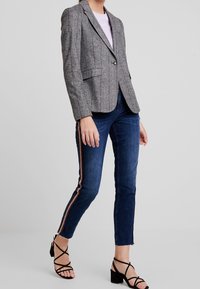 Grå rutigt kavaj med en figursydd design, enkel knappstängning och två framfickor, matchad med mörka denimjeans som har sidostripes.