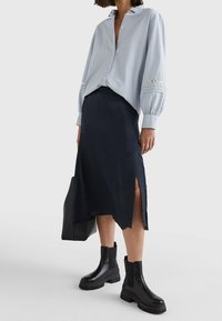 Gestreept blauw overhemd met ballonsleeves, gecombineerd met een marineblauwe mid-length rok met zijsplitten, aangevuld met zwarte enkellaarsjes.