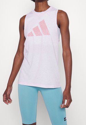 Persoon draagt een lichtroze mouwloos topje met een vervaagd roze Adidas-logo en lichtblauwe nauwsluitende fietsbroek.