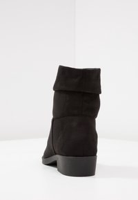 Bottine en suède noir avec un revers replié, semelle en caoutchouc et un talon bas texturé. Présente une finition lisse et mate et un design simple.