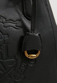 Mustan nahkainen käsilaukku, jossa on teksturoitu pinta, kohokuvioitu logo ja kultainen metallirengas, johon on kiinnitetty nahkahihna.