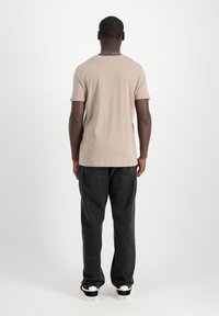 Bežs īsās piedurknes T krekls, izgatavots no kokvilnas, kopā ar vaļīgām melnām džinsām. Apģērbs izceļas ar minimālistisku dizainu un neitrālu krāsu paleti.