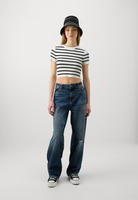 Svart-og-hvitt-stripet kort topp, høyt liv blå jeans med slitte detaljer, og svart bøttehatt, kombinert med svarte joggesko.