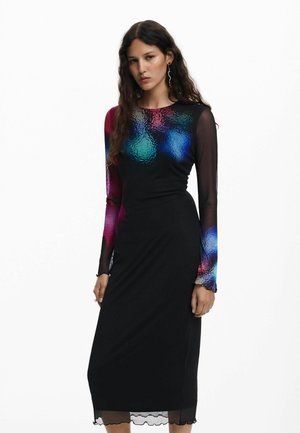 Mujer vistiendo un vestido midi negro con mangas largas transparentes y patrones abstractos coloridos en azul, rojo y verde en la parte superior del pecho y las mangas.