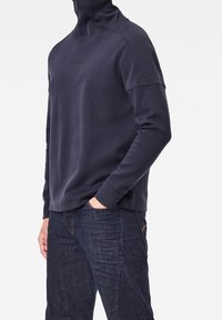 Felpa a collo alto blu navy realizzata in tessuto morbido, con design senza cuciture, branding minimalista sul petto e maniche lunghe.