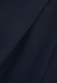 Tessuto blu scuro con una texture liscia, che mostra pieghe e cuciture sottili. Il materiale appare resistente e ben strutturato.