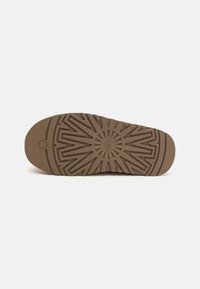 Semelle de chaussure en caoutchouc marron présentant un motif géométrique avec des accents en relief. Le design inclut un logo central et une surface texturée pour une meilleure adhérence.
