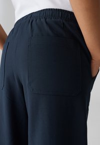 Pantalons larges bleu marine avec une taille élastique, comportant une poche arrière carrée et un tissu lisse et texturé.