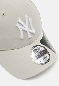 Lyse grå baseballcaps med hvit brodert "NY"-logo, justerbar stropp, og et blankt rundt merke som identifiserer det som en New Era 9FORTY-modell.