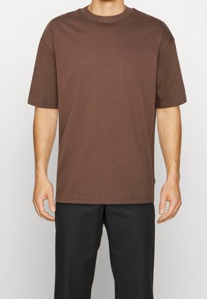 Brown cotton t-shirt with short sleeves, round neckline, and a relaxed fit, worn over black pants, featuring a simple design and no patterns.