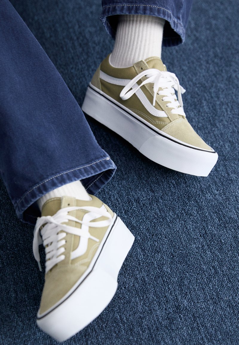 Zapatillas de plataforma de ante verde con detalles en blanco, cordones y suelas de goma, combinadas con pantalones de mezclilla azules y calcetines blancos acanalados.