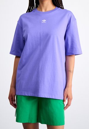 T-shirt en coton violet à manches courtes et col rond. Présente un petit logo blanc d'adidas sur la poitrine. Associé à un short vert.