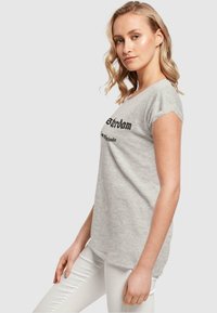Tricou gri cu mâneci scurte, cu text negru care scrie "Amsterdam" și "Olanda", fabricat dintr-un material moale; croi normal cu guler rotund.