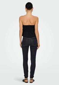 Top strapless negro con fruncidos combinado con jeans oscuros ajustados, que muestran una silueta elegante y un diseño sencillo. Sandalias planas completan el look.