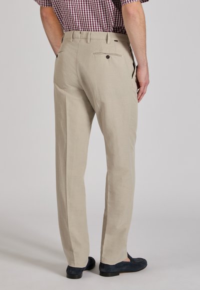 Beżowe lniane spodnie o prostym kroju, z tylnymi kieszeniami zapinanymi na guziki. Noszone z ciemnymi zamszowymi mokasynami.