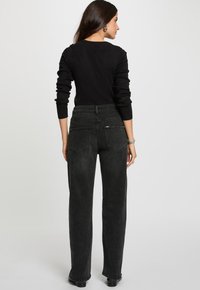 Haut noir à manches longues associé à un jean taille haute gris foncé. Les jeans présentent des poches arrière et un design droit. Texture de tissu lisse.