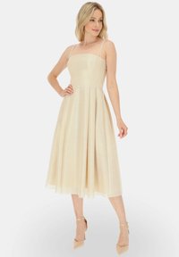 Beżowa sukienka w kształcie litery A z cienkimi ramiączkami, dopasowanym gorsetem i rozkloszowaną spódnicą sięgającą do połowy łydki, wykonana z błyszczącego, teksturowanego materiału.