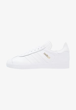 Baskets blanches Adidas Gazelle avec lettrage doré, fermeture à lacets et semelle en caoutchouc texturée, vues de côté extérieur.