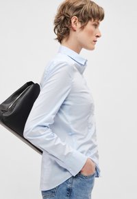 Svetlomodrá košeľa s dlhým rukávom a golierom na gombíky, vyrobená z hladkej látky, nosená s rifľovinou a držiaca čiernu kabelku.