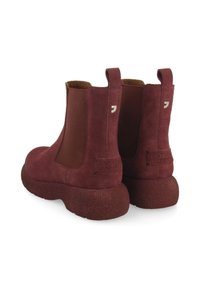Bottines en daim bourgogne avec panneaux latéraux élastiques, semelle épaisse et texturée, marque minimaliste sur le talon et languettes de tirage pour un enfilage facile.