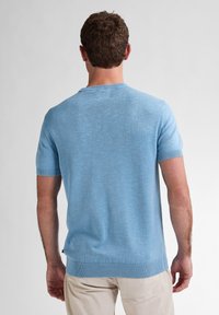 Pulover scurt cu mânecă scurtă, de culoare bleu deschis, cu guler rotund. Materialul pare texturat și respirabil, având accente cu dungi la manșete și pe margine.