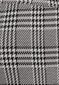 Tissu présentant un motif géométrique en noir et blanc, avec des motifs en zigzag et à carreaux créant un design texturé et contrasté.