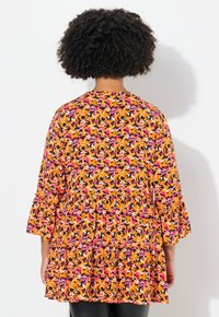 Blumenmuster-Kleid in Orange, Pink, Schwarz und Weiß. Mit ausgestellten Ärmeln und einem gestuften Design, aus leichtem Stoff gefertigt.